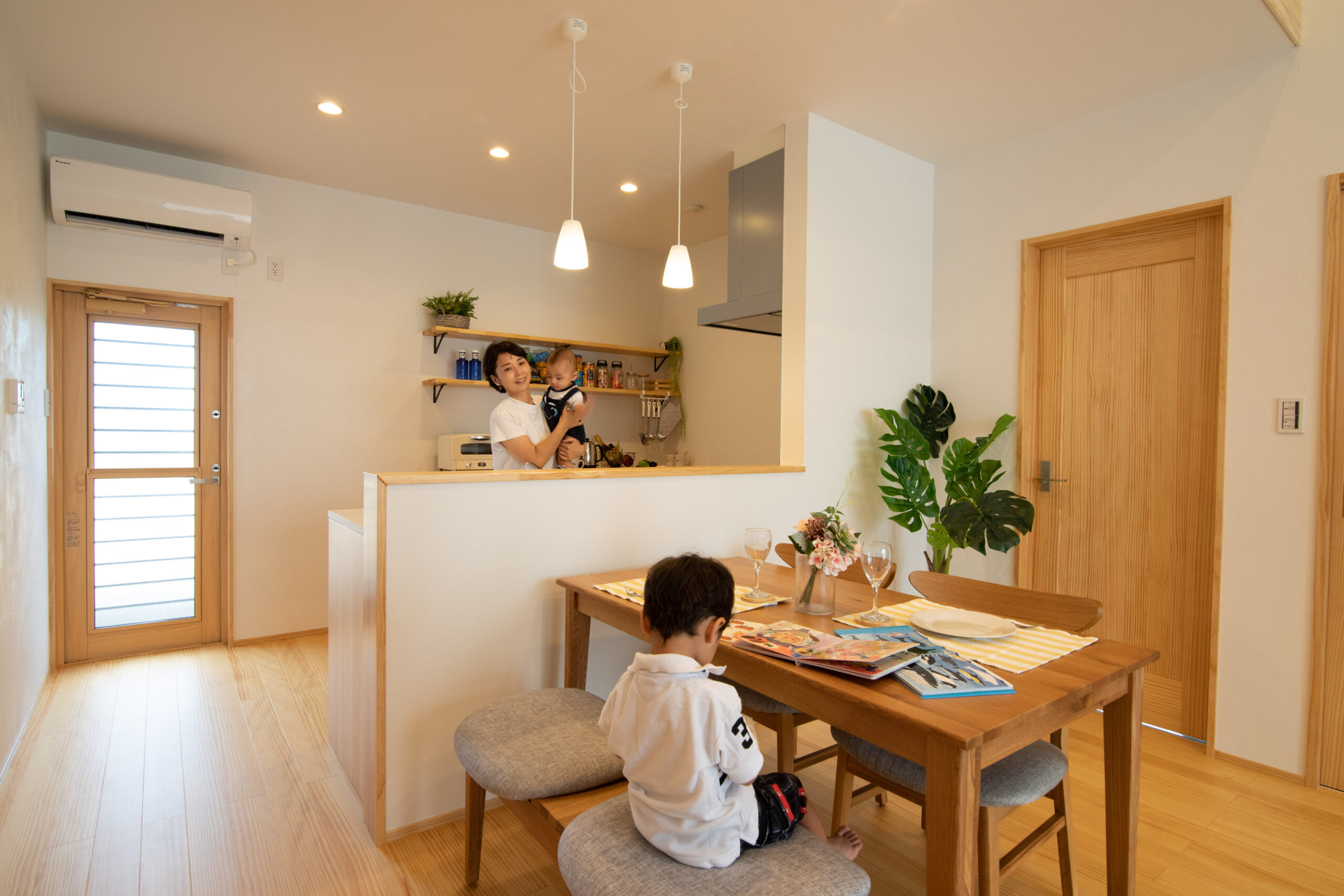 ナチュラルテイストのダイニングで勉強するこどもとそれをキッチンから見守るお母さん（アイラックホーム施工事例）.jpg